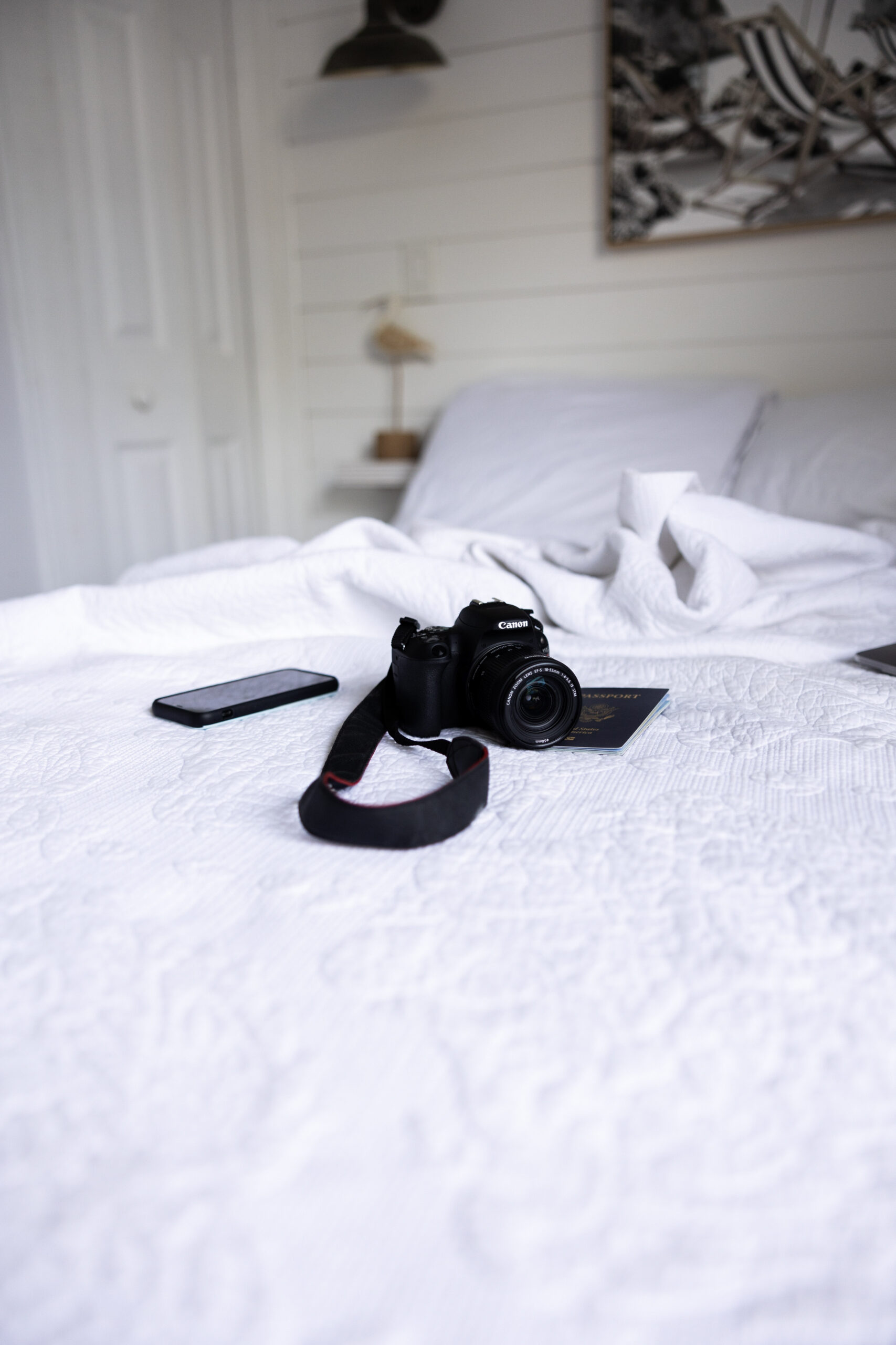 cannon camera sitting on a full size bed with white sheets and a phone placed next to the camera